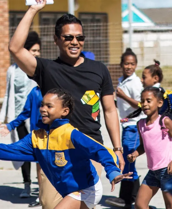 Norbert Elnar laughing and playing with a group of children outdoors.